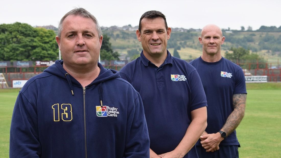 3 middle aged men standing in a rugby pitch looking at camera