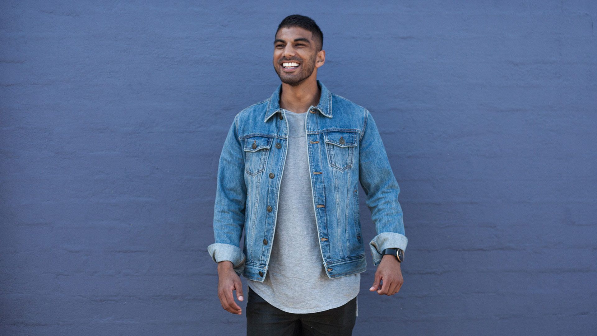 Mo Bro Roshan standing against a painted brick wall smiling