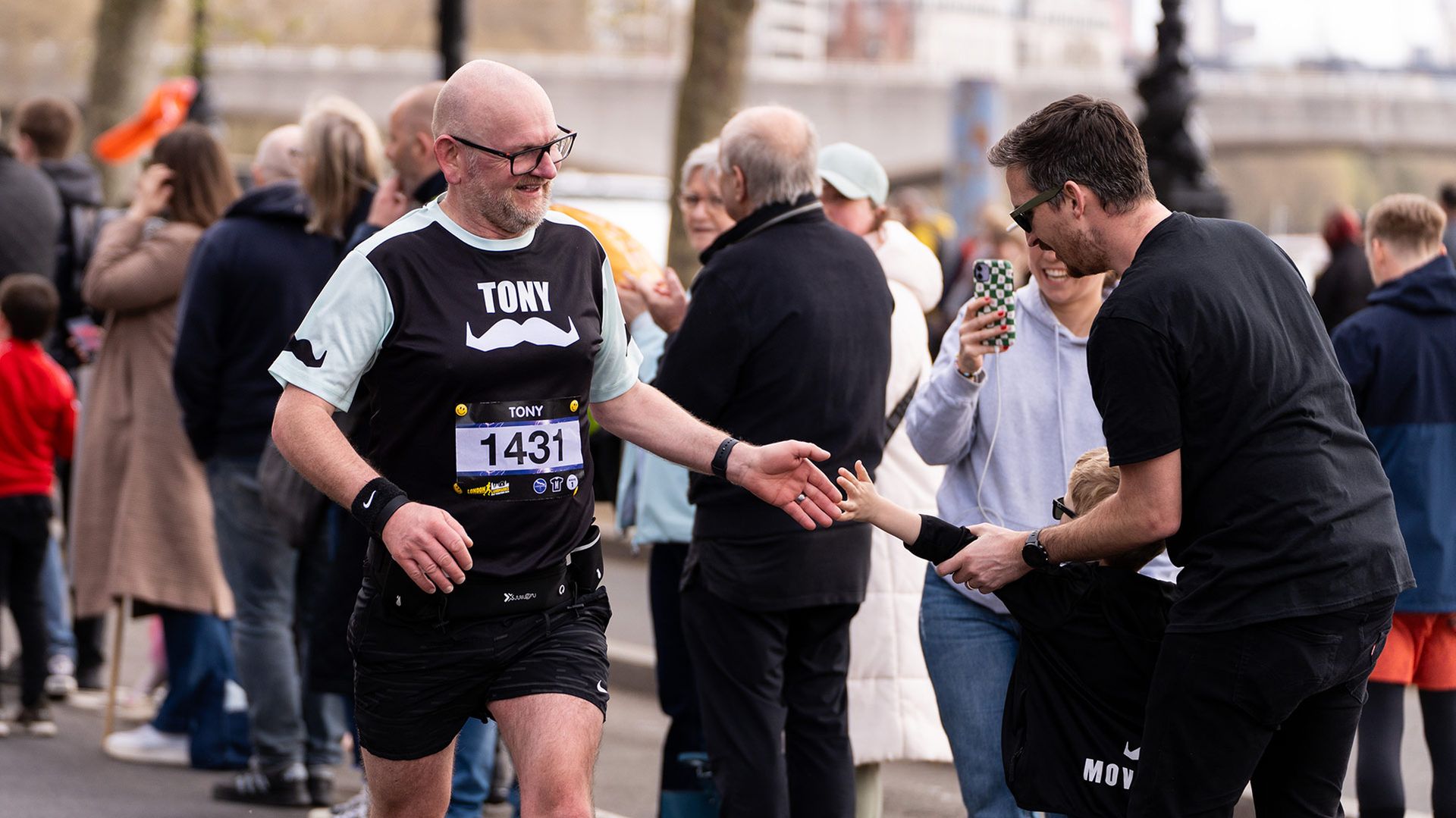 Photo of a runner at a marathon receiving congratulations from a child in the crowd.