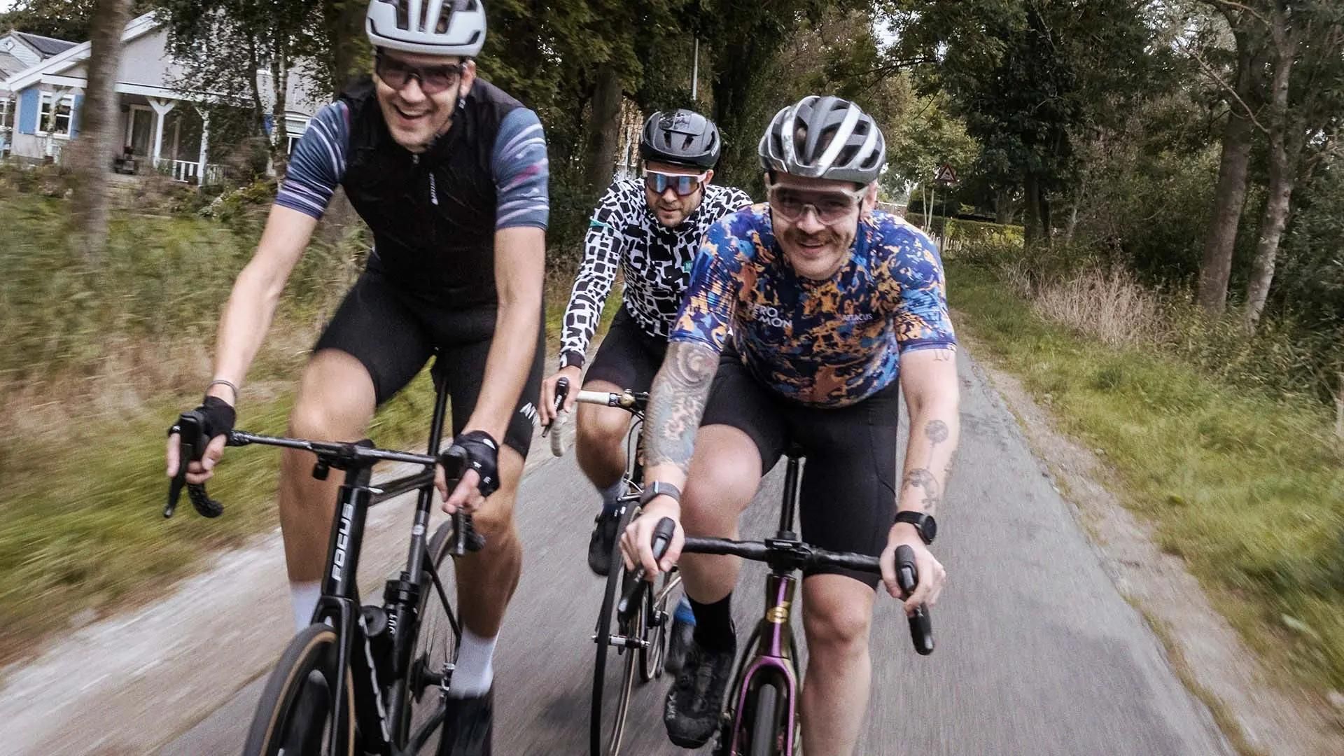 Athletic bicycle riders, in riding gear, smiling and speeding toward camera.